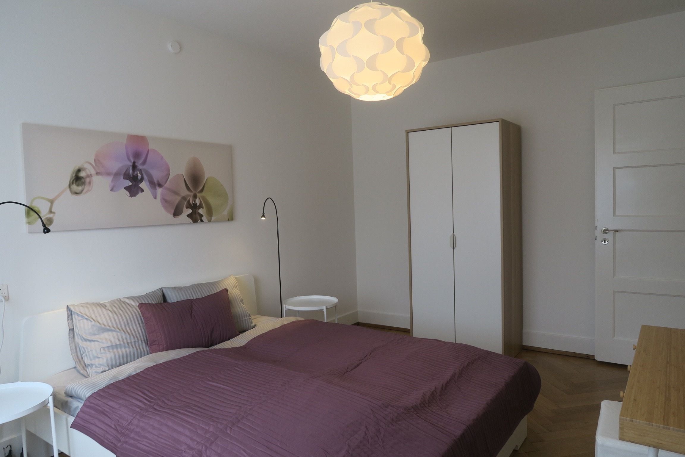 A bedroom with a bed, a bedside table, a wardrobe, and a wall-mounted light fixture.