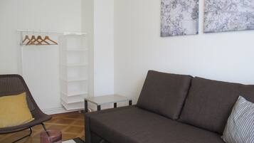 Uma sala de estar moderna com um sofá cinzento, uma cadeira de vime com uma almofada amarela, uma pequena mesa branca e um castiçal de vidro.