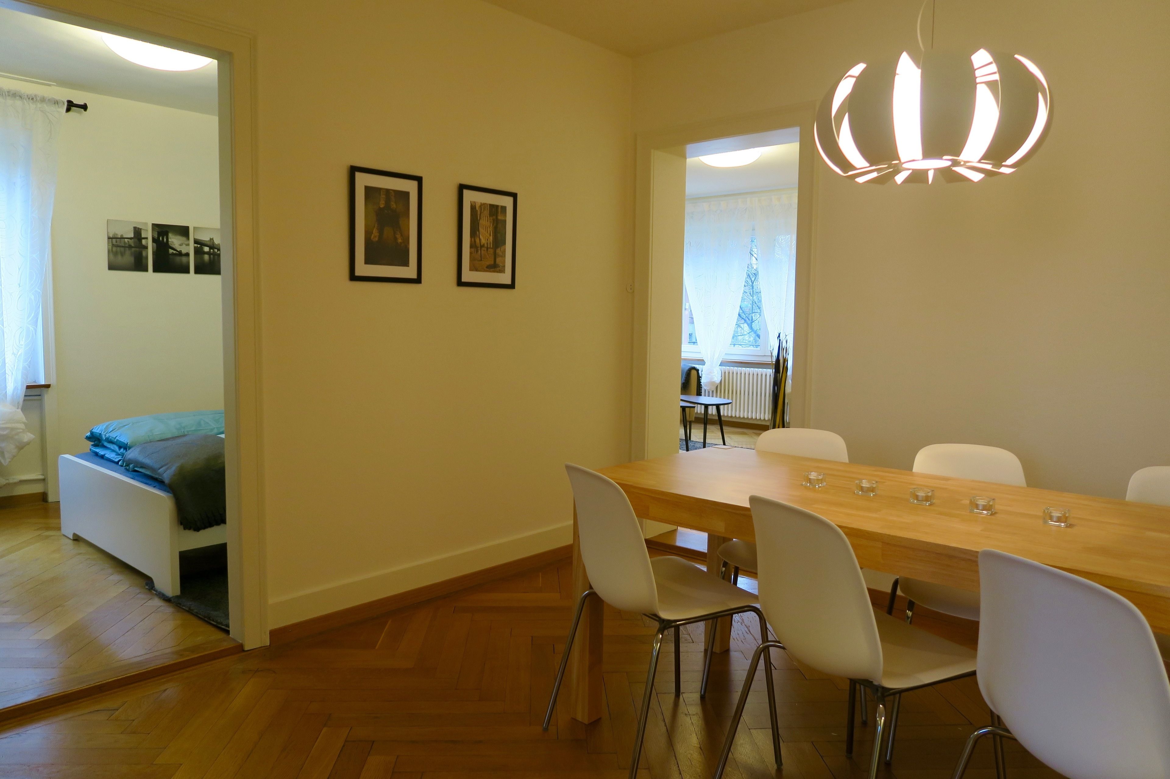 A dining area with a wooden table and white chairs, a chandelier, and framed pictures on the wall.