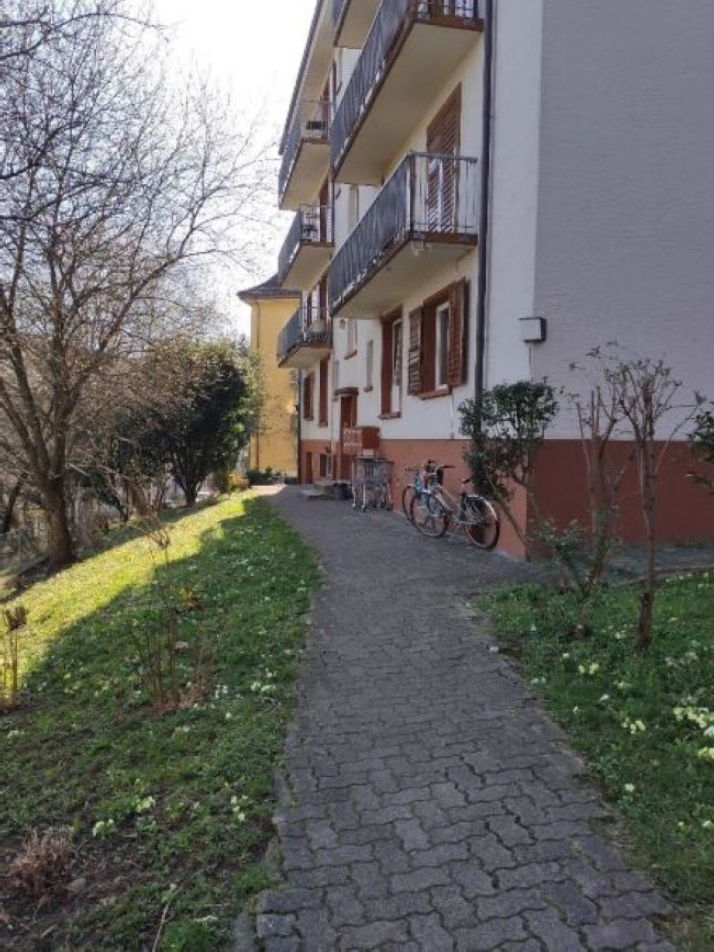 A pathway leading to a multi-story building with balconies and bicycles parked outside.