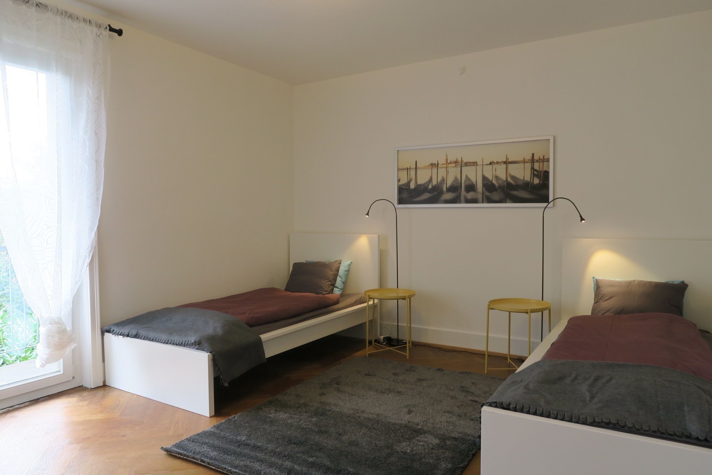 Un dormitorio con dos camas individuales, una mesita, una silla y una ventana con cortinas.