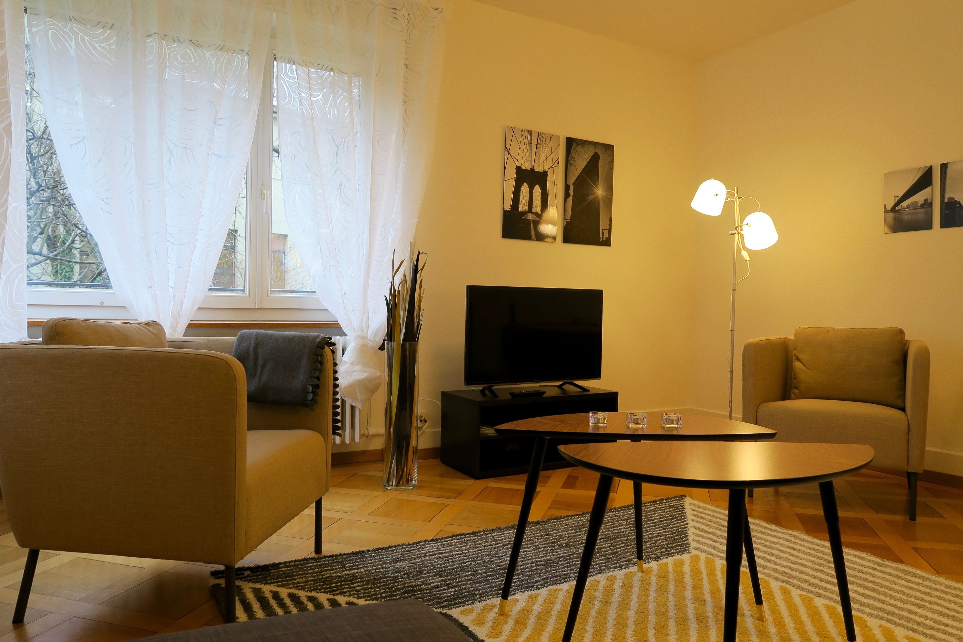 Un salon moderne avec un canapé, un téléviseur, une table basse et une lampe.