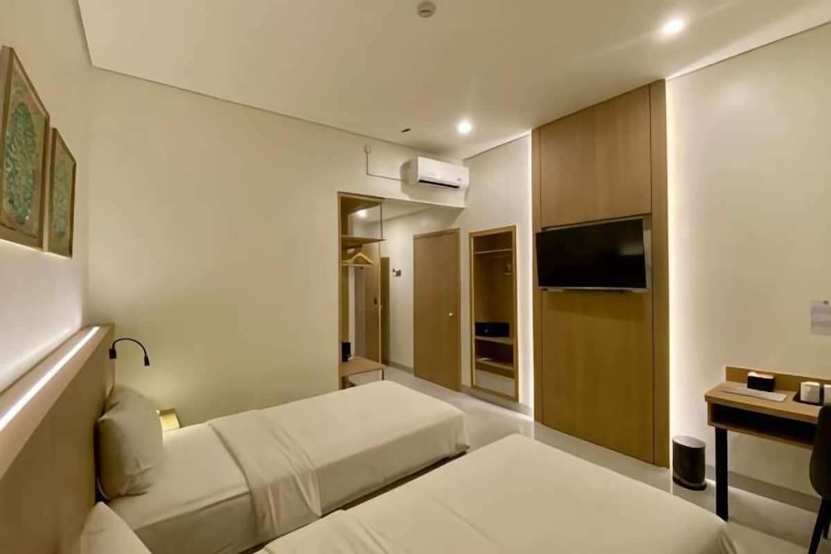 Ein Hotelzimmer mit zwei Betten, einem Schreibtisch, einem Fernseher, einem Kleiderschrank und einer Klimaanlage.