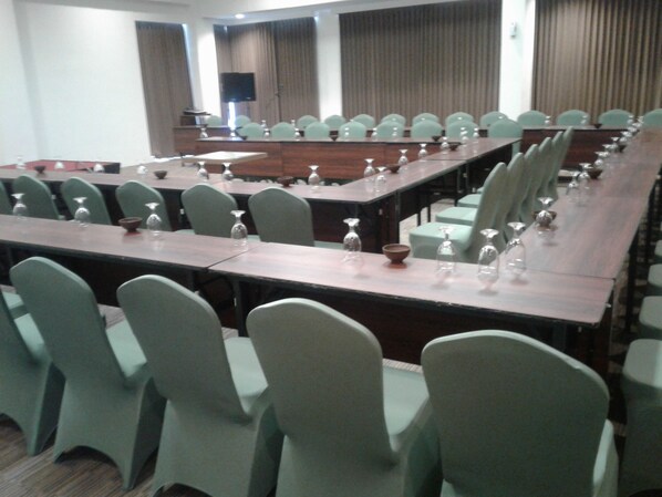 Un salón de conferencias con largas mesas y sillas, equipado con vasos de agua y una televisión de pantalla plana.