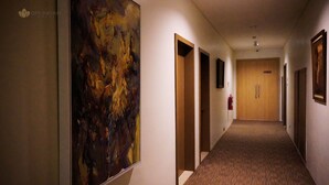 A hotel hallway with a large abstract painting on the left, wooden doors, and a fire extinguisher mounted on the wall. - Opi Indah Hotel (Palembang)