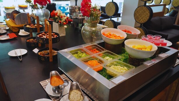 A buffet with various food items and a vase of flowers. - Opi Indah Hotel (Palembang)