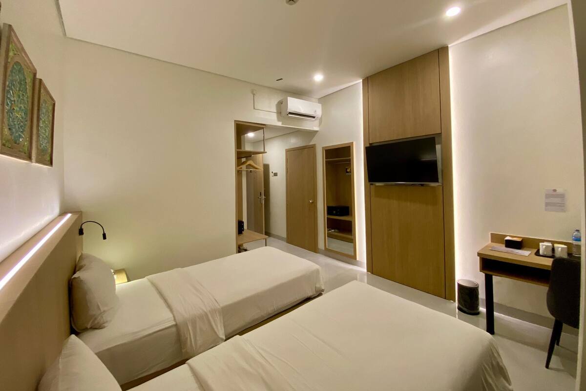Ein Hotelzimmer mit zwei Betten, einem Schreibtisch, einem Fernseher und einem Kleiderschrank.