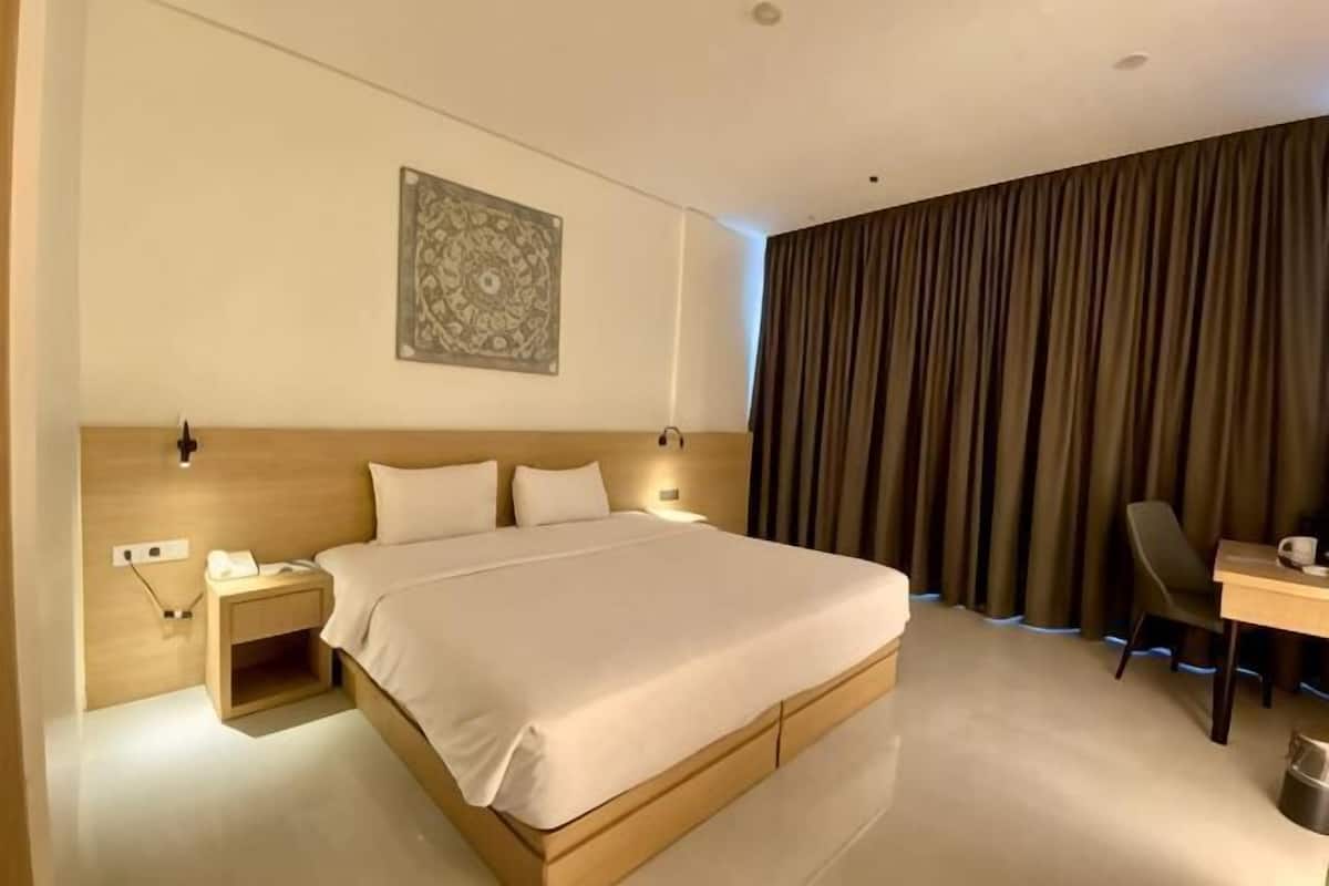 Ein Hotelzimmer mit einem großen Bett, Nachttischen, einem Schreibtisch und einem fensterbedeckenden Vorhang.
