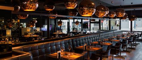A restaurant with a long counter, booths, and hanging spherical light fixtures.