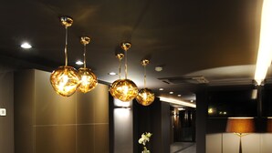 A modern reception area with a curved reception desk, multiple pendant lights, and a floor lamp. - Hotel Le Florentin (Florenville)