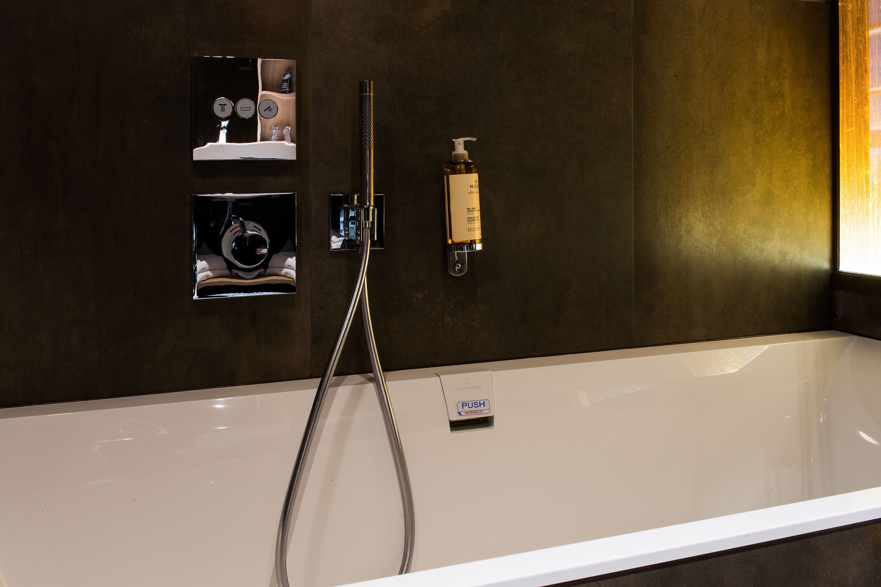 Un baño moderno con una bañera grande, un cabezal de ducha de mano, un dispensador de jabón en la pared y un estante pequeño con artículos de aseo.