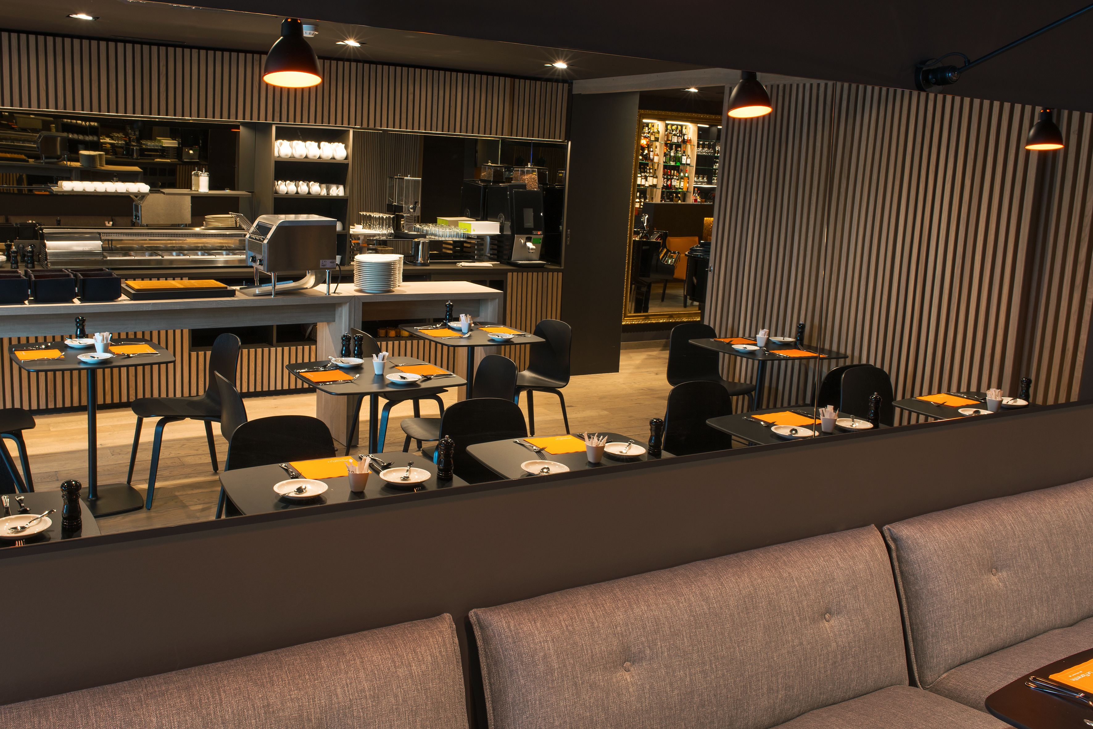Un restaurante moderno con zona de bar, mesas y sillas, y una barra con máquina de café.