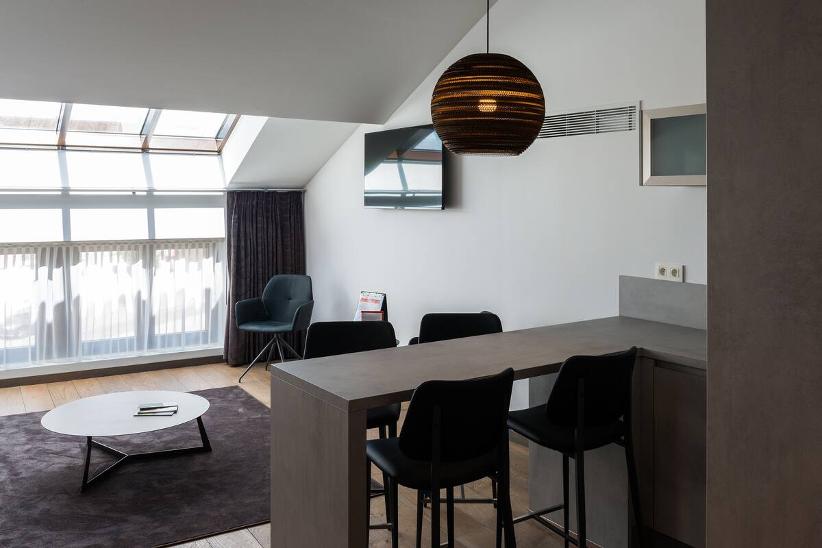 A modern kitchen with a dining area, large windows, and a hanging light fixture.