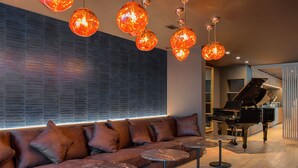 A modern lounge area with a brown leather sofa, round tables, and a grand piano. - Hotel Le Florentin (Florenville)