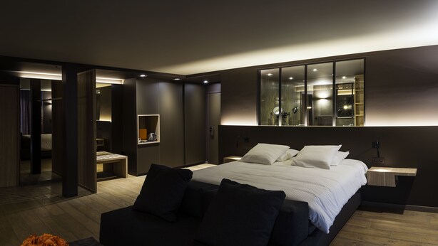 A modern bedroom with a large bed, bedside tables, a mirror, and a wooden floor. - Hotel Le Florentin (Florenville)