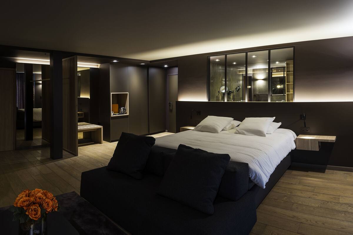 A modern bedroom with a large bed, bedside tables, a mirror, and a wooden floor.