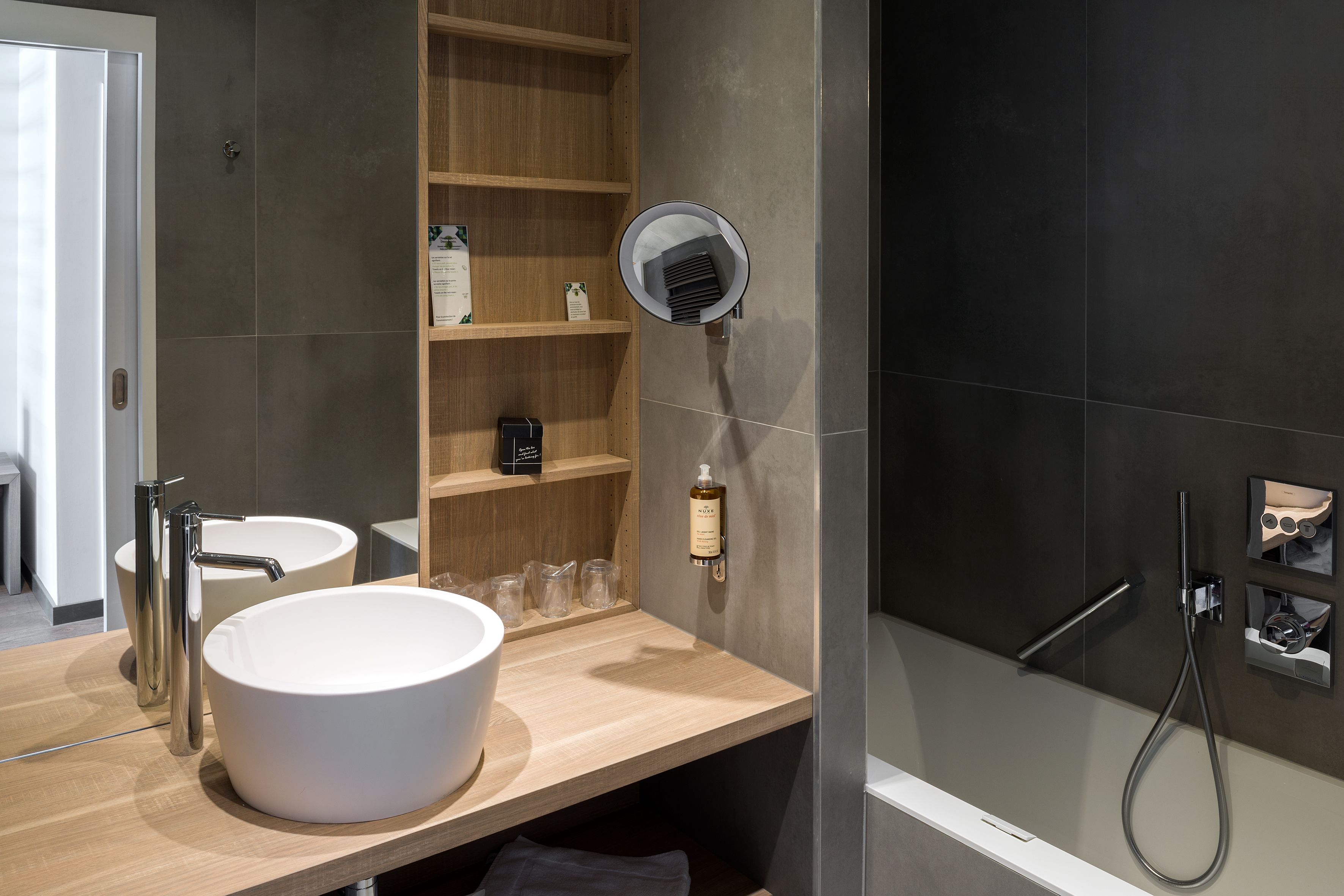 A modern bathroom with a large white sink, a handheld showerhead, and a built-in mirror.