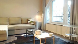 A modern living room with a sofa, a coffee table, a lamp, and a view of the city through large windows.