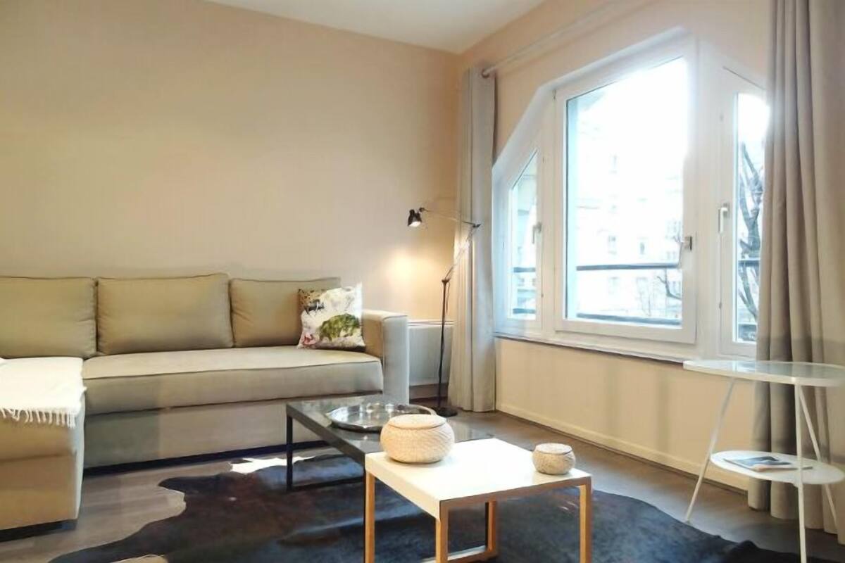Ett modernt vardagsrum med en soffa, ett soffbord, en lampa och utsikt över staden genom stora fönster.