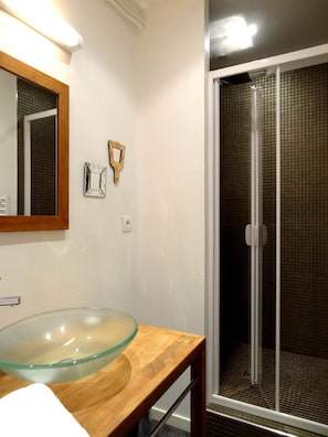 Un baño con un lavabo de cristal, un mueble de tocador de madera, un espejo y una cabina de ducha de cristal.