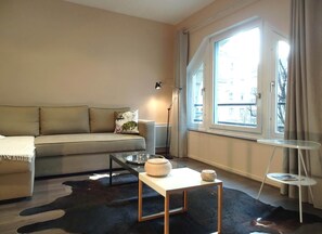 Una sala de estar moderna con un sofá, una mesita, una lámpara y vistas de la ciudad a través de amplias ventanas.