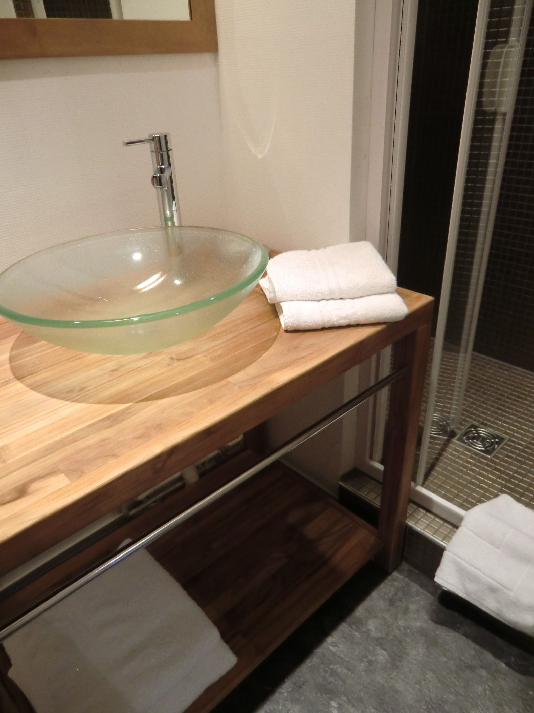 A modern bathroom with a glass bowl sink, wooden vanity, and a shower area.