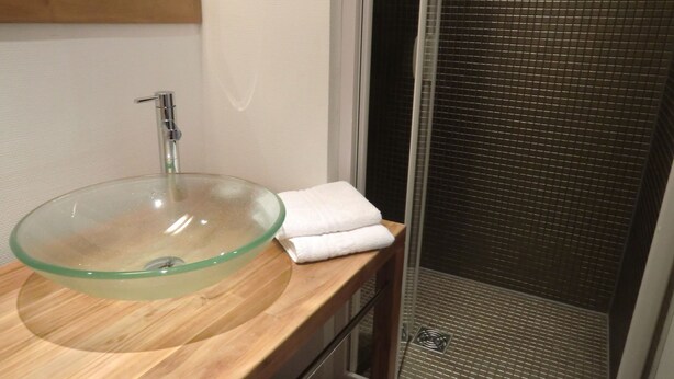 A bathroom with a glass sink, wooden countertop, and a shower area with a tiled floor.