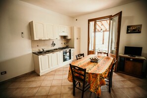 Cocina compacta con armarios blancos, estufa y una mesa de comedor con mantel floral.