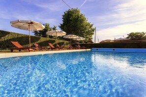 A swimming pool with clear blue water, surrounded by lounge chairs and umbrellas. - Casa Vacanze Ribocchi (Campiglia Marittima)