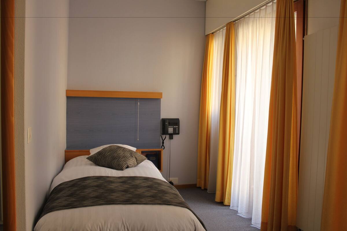 A hotel room with a bed, a bedside telephone, and curtains.