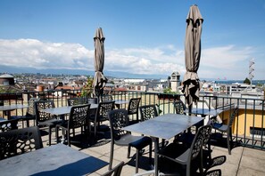 Una terrazza sul tetto con tavoli e sedie, ombrelloni e vista sulla città.