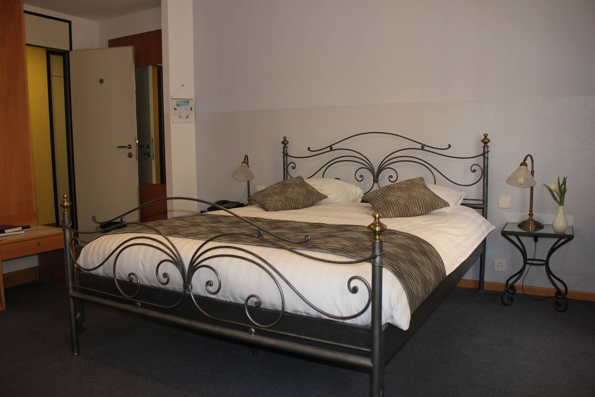 A neatly made bed with a metal frame, two bedside tables with lamps, and a wooden desk.