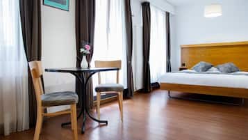 A hotel room with a wooden bed, a small table with chairs, a vase with flowers, and a view of the city through the window.