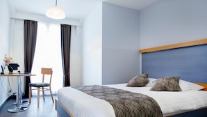A hotel room with a large bed, a desk with a chair, and a window with curtains. - Hotel Bel'Espérance (Geneva)