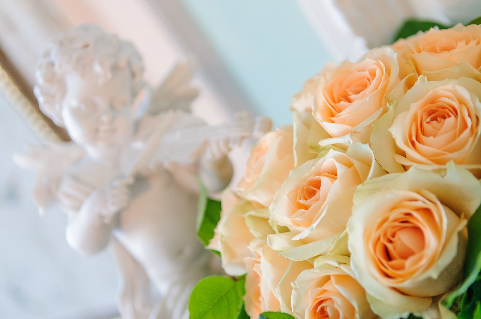 A statue of a cherub holding a bouquet of peach-colored roses.