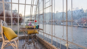 Una habitación con una mesa dispuesta para dos personas, una silla con cojín amarillo y vistas a un río con edificios al fondo.