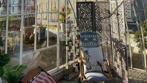 Un invernadero con techo de cristal, una silla de madera y un panel decorativo.