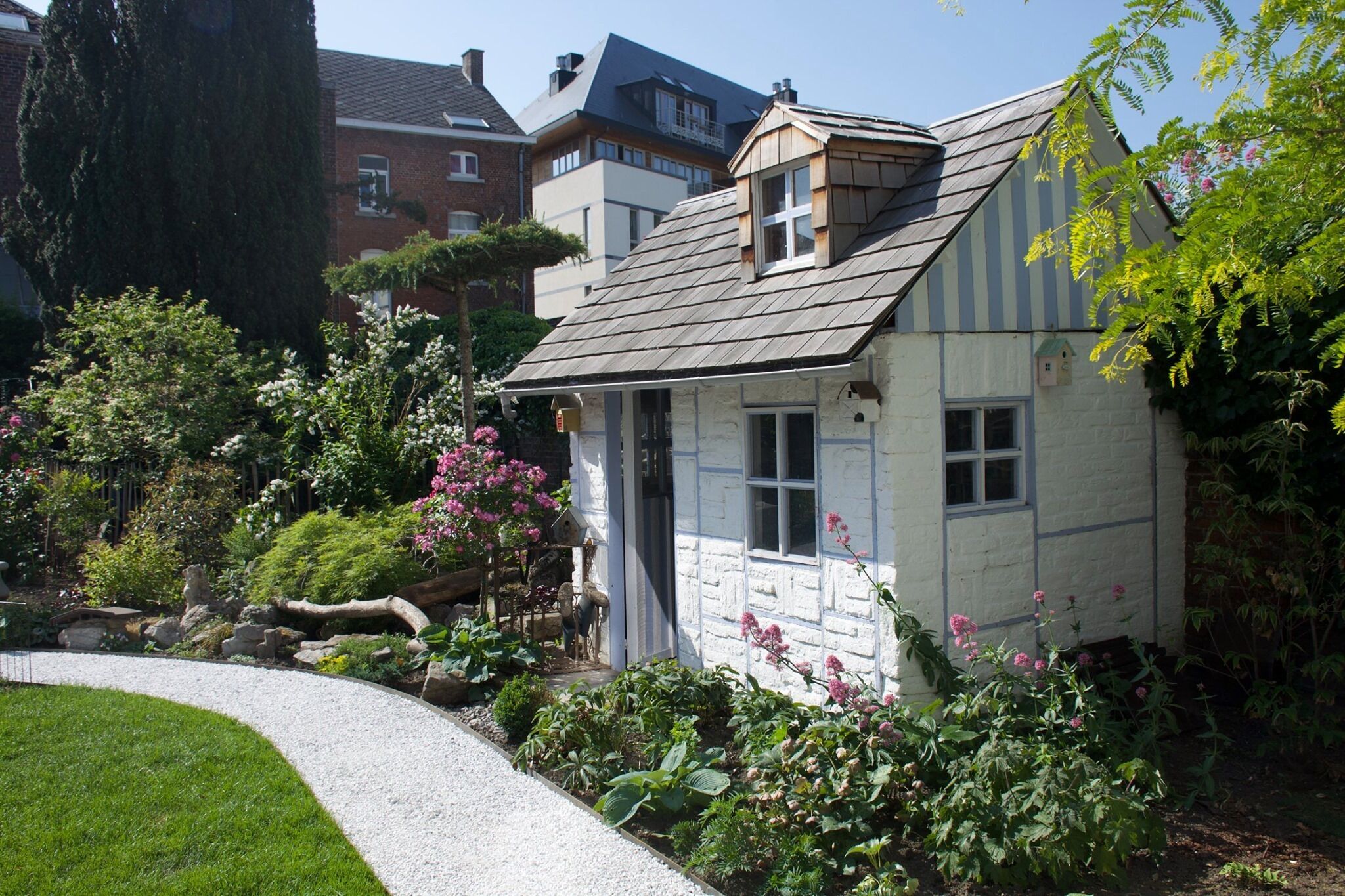 Un pintoresco cottage con techo inclinado, rodeado de un jardín bien cuidado con diversas plantas y flores.