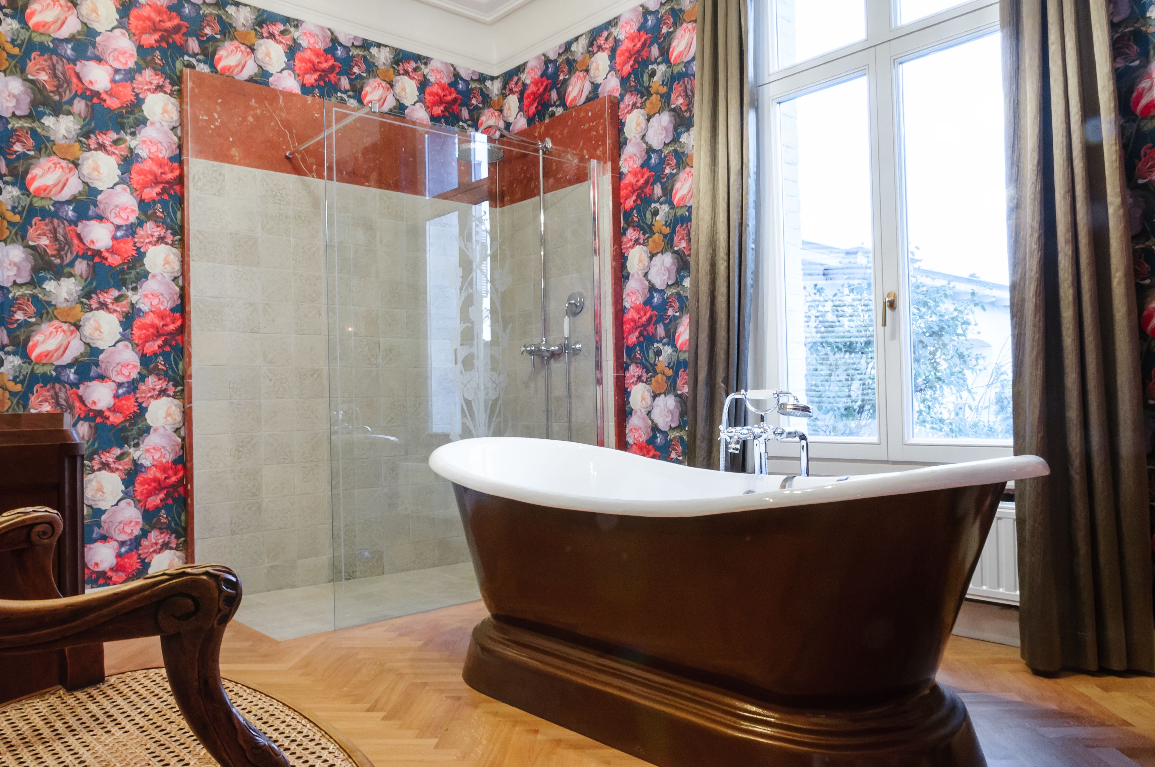 A bathroom with a freestanding bathtub, a glass-enclosed shower, and floral wallpaper.