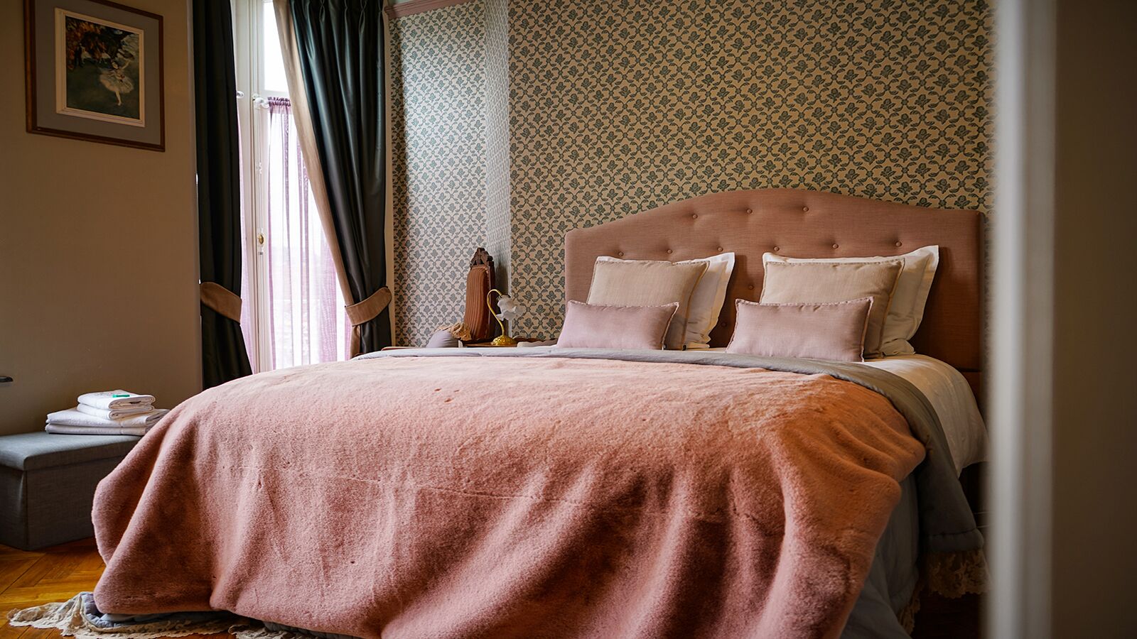 A bedroom with a large bed, a bedside table, a lamp, and a patterned wallpaper.