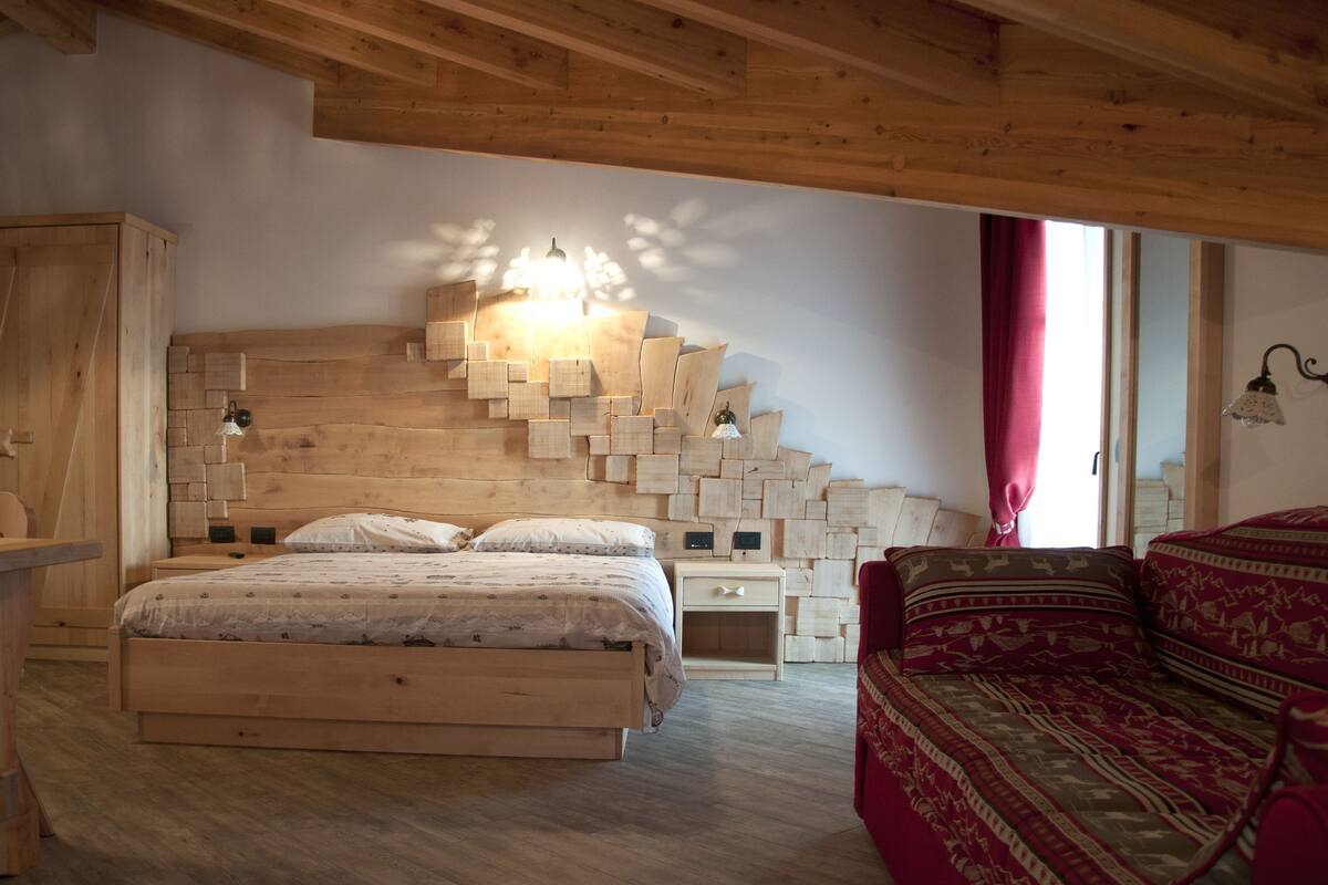 Un dormitorio de madera con cama, mesitas de noche, armario y ventana con cortinas.