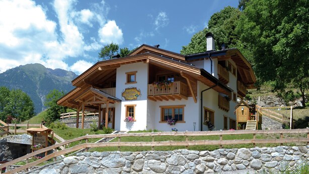 A traditional chalet with a stone wall, wooden balcony, and a mountain backdrop. - Dalla Natura la Salute (Giustino)