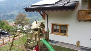 A wooden play structure with a slide, a swing, and a climbing area, adjacent to a house with a window and a balcony. - Dalla Natura la Salute (Giustino)