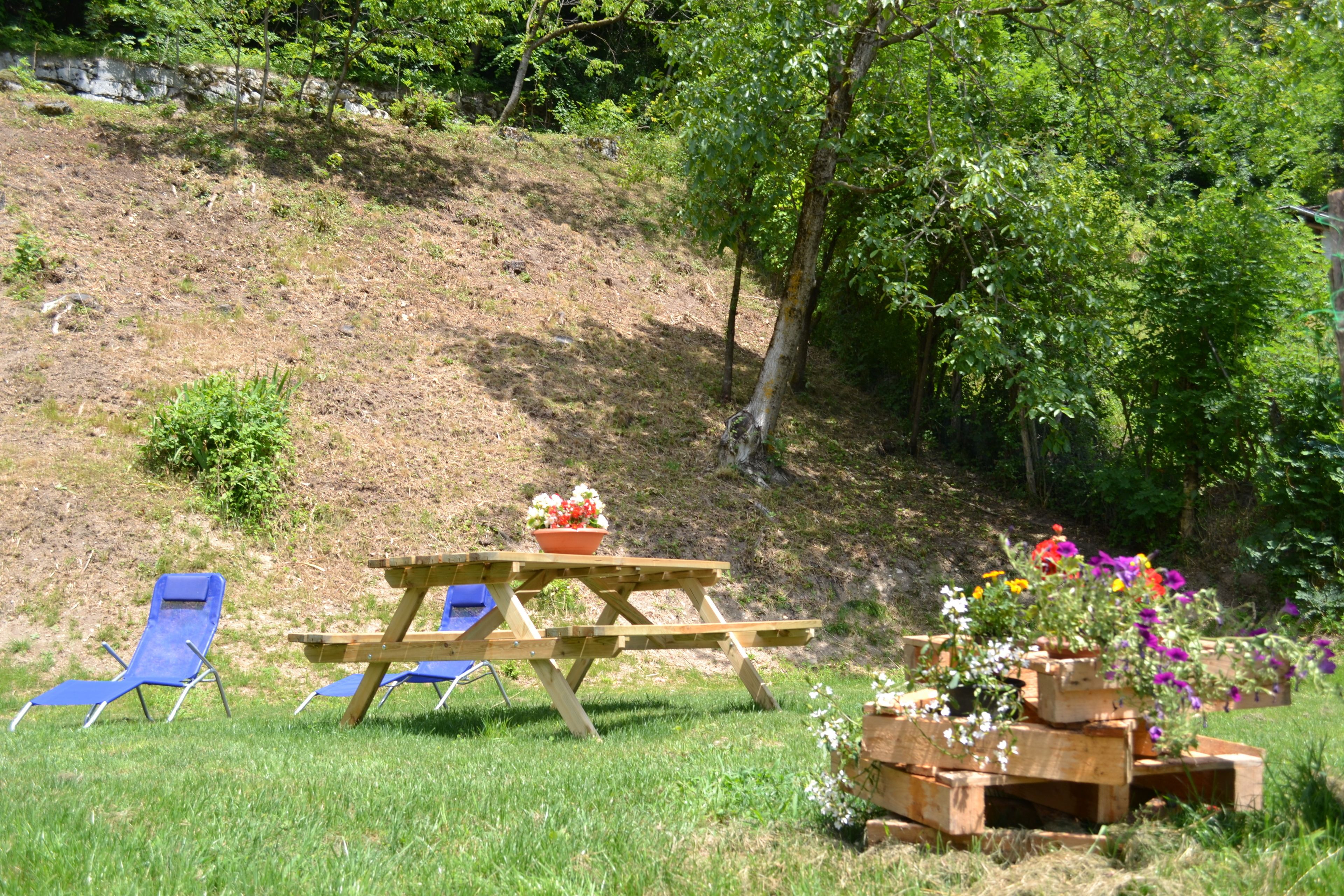 A picnic setup with a wooden table and blue chairs on a grassy hill.