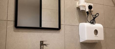 A modern bathroom with a large mirror, a vessel sink, and a hand dryer.