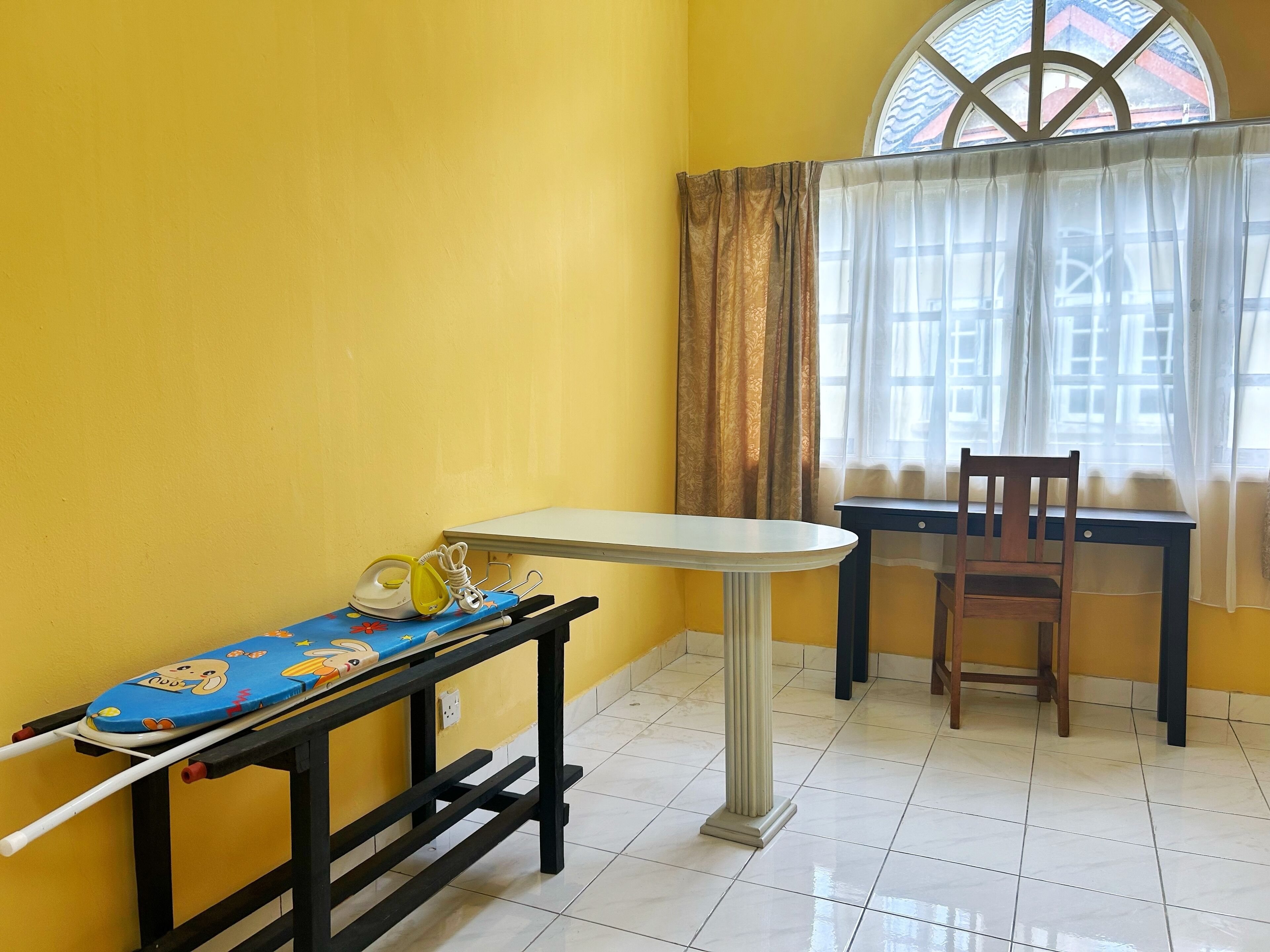 A room with a yellow wall, a table with a blue tablecloth, a chair, and a window with curtains.