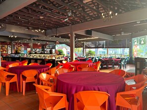 A restaurant with multiple tables and chairs, a bar area, and large windows offering a view of the outside.