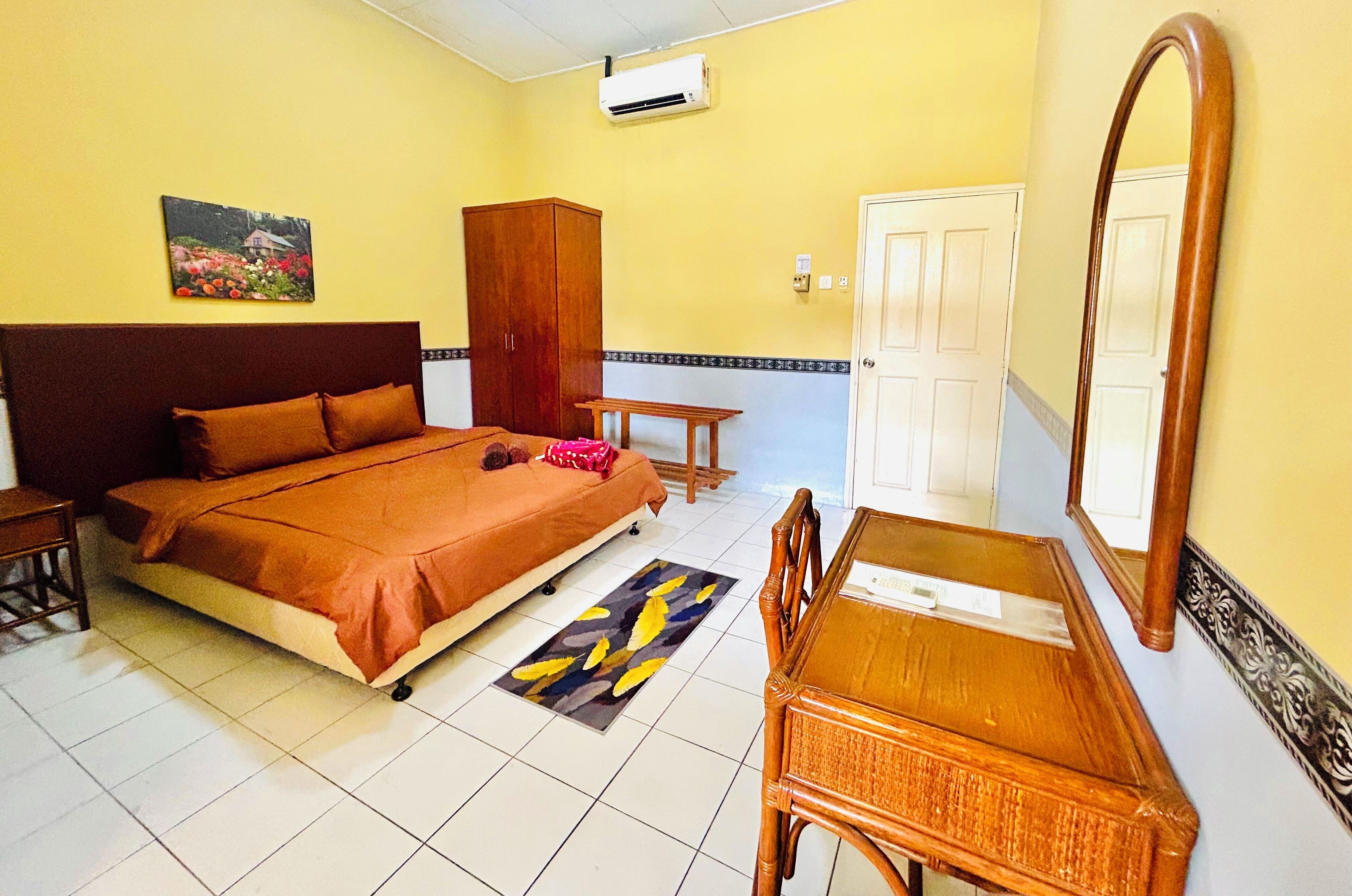 A bedroom with a bed, a wooden wardrobe, a small table, a chair, a mirror, and a door.
