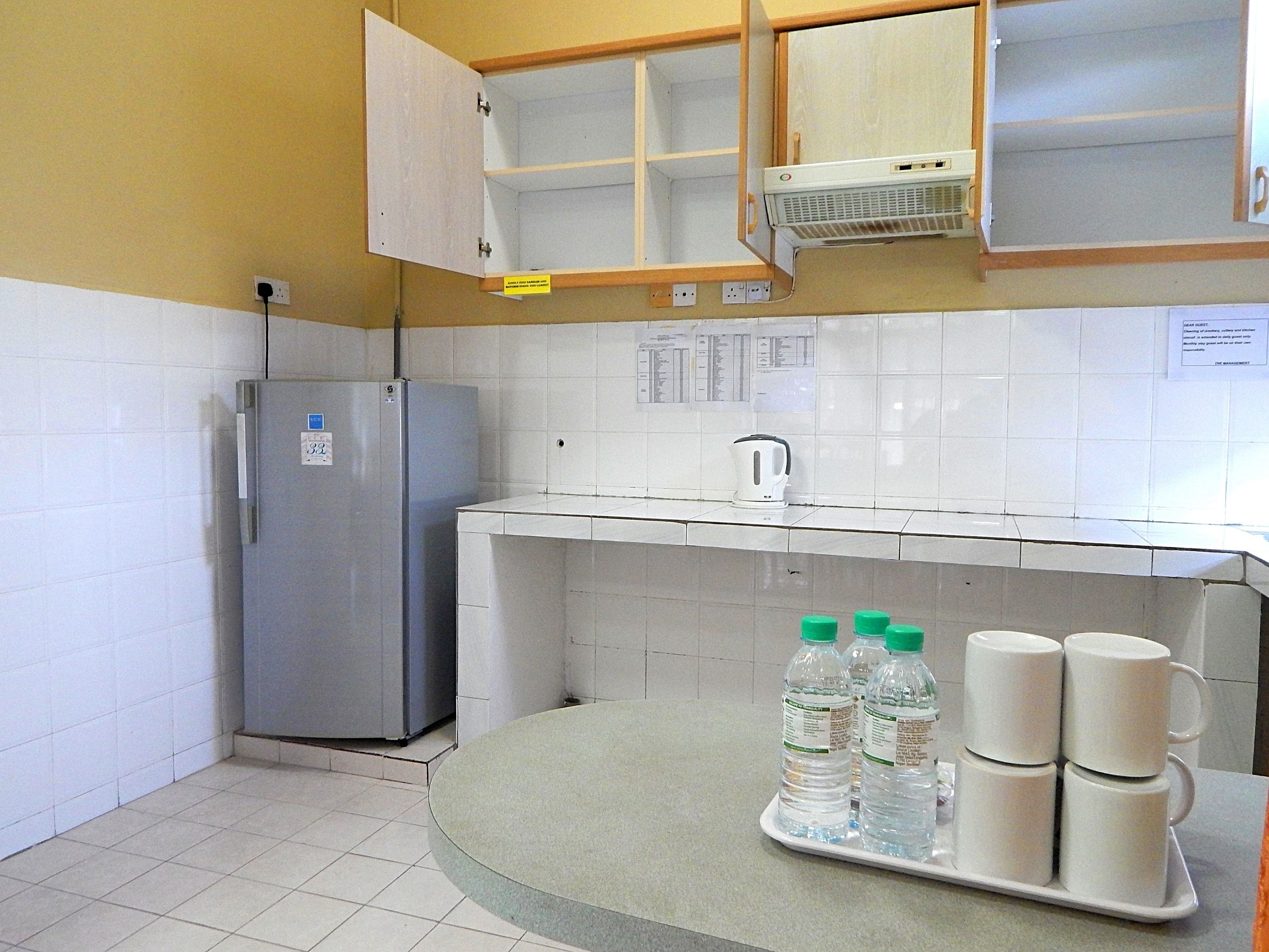 Een kleine keuken met een koelkast, een spoelbak en een klein aanrecht. Er staan waterflessen en bekers op het aanrecht.