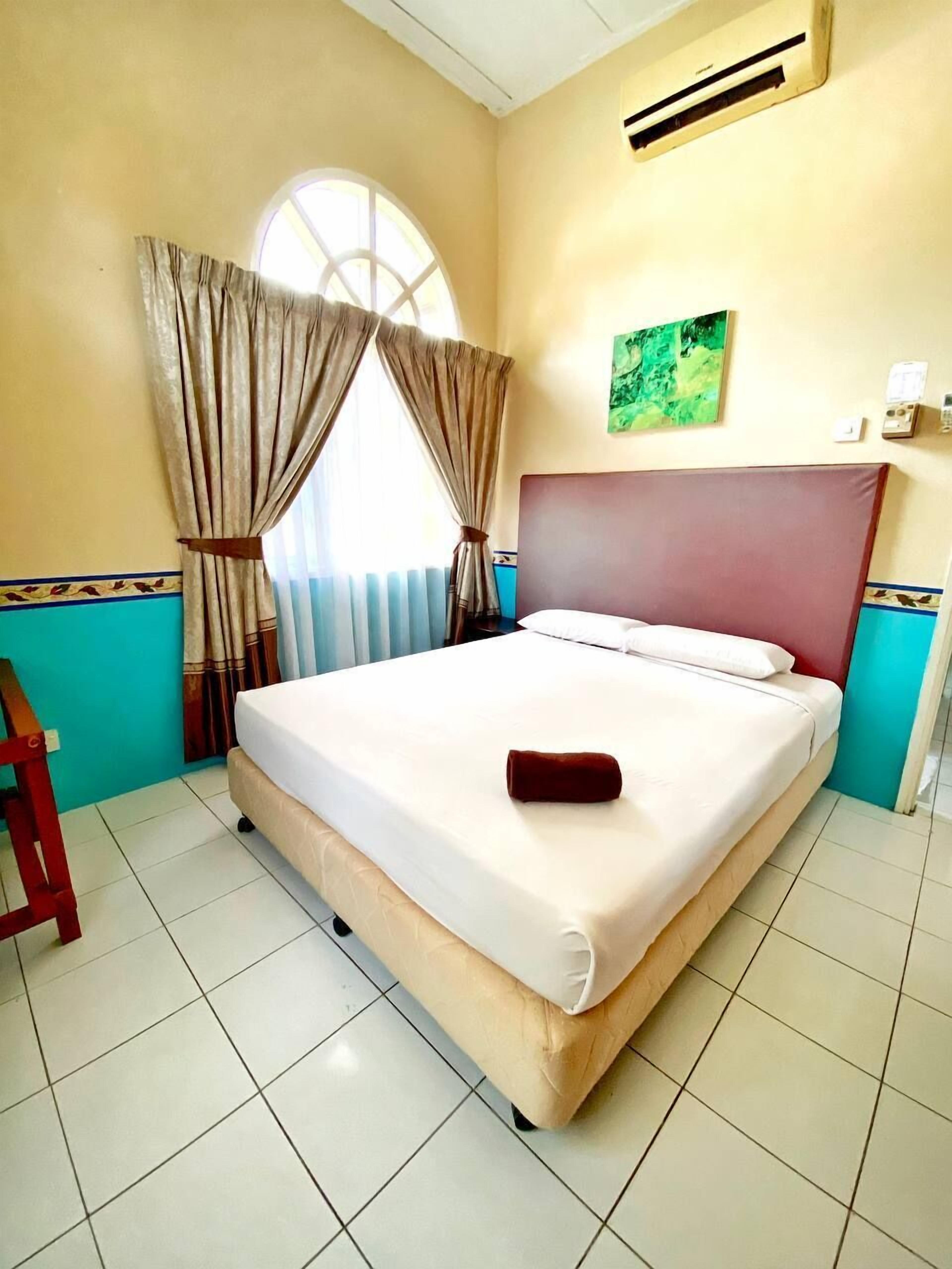 Une chambre d’hôtel avec un lit, des rideaux, une fenêtre, un appareil de climatisation et une petite table.
